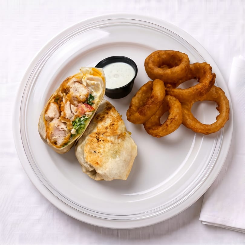 Chicken wrap cut in half with lettuce and tomato, onion rings, and dipping sauce on a white plate.