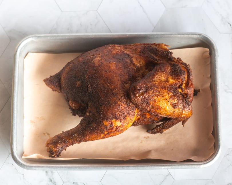 Spatchcocked roasted chicken with dark, crispy skin in a metal pan.