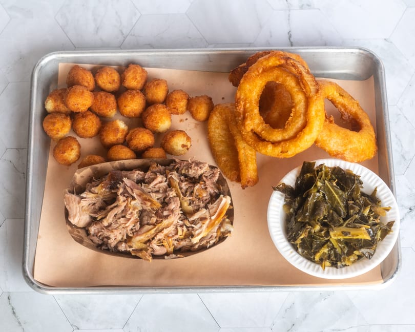 Barbecue platter with pulled pork, hush puppies, onion rings, and collard greens.