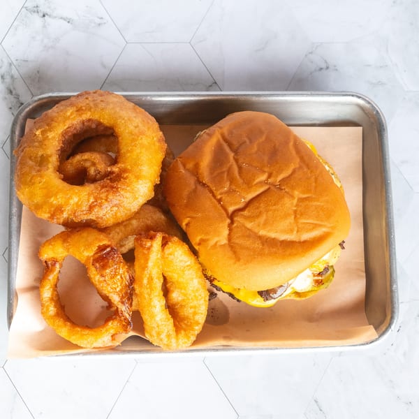 Cheeseburger with melted cheese, fries, and golden onion rings served on a parchment-lined metal tray.