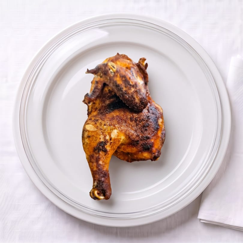 Crispy, golden-brown roasted chicken on a simple white plate.